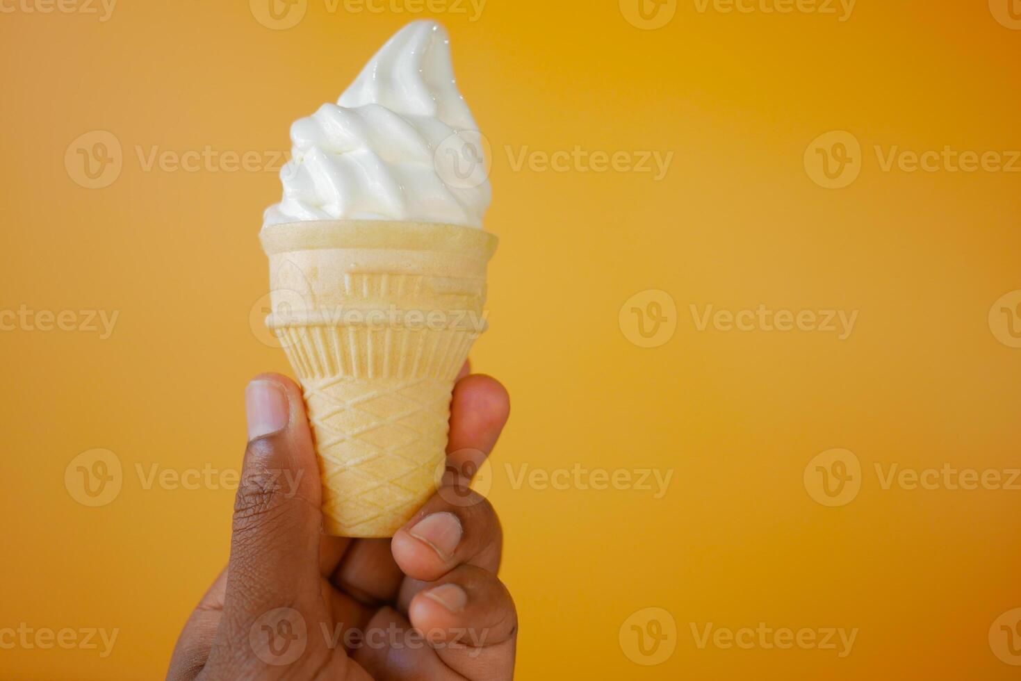 Hand Holding Vanilla Soft Serve Ice Cream Cone against Vibrant Orange Background photo