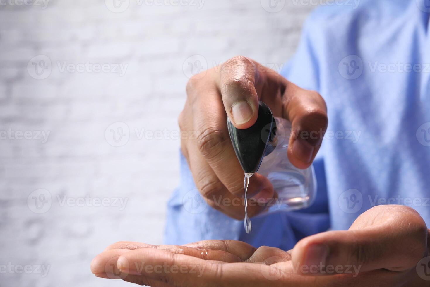 A person wearing a blue shirt is using hand sanitizer from a bottle for cleanliness and hygiene photo