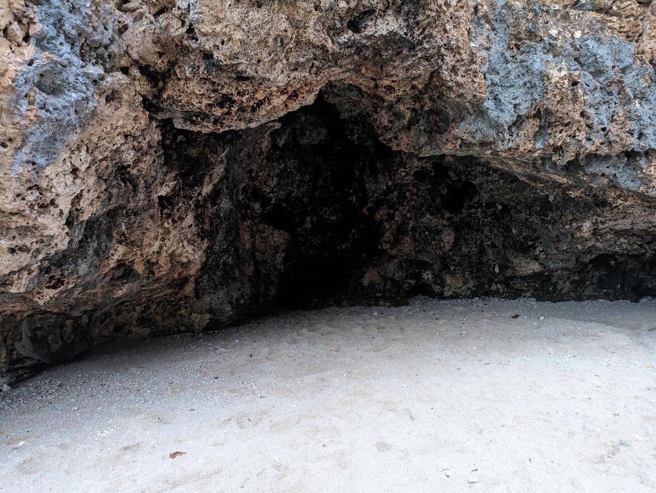 A cave entrance on a sandy beach with blue waves crashing in the background. photo