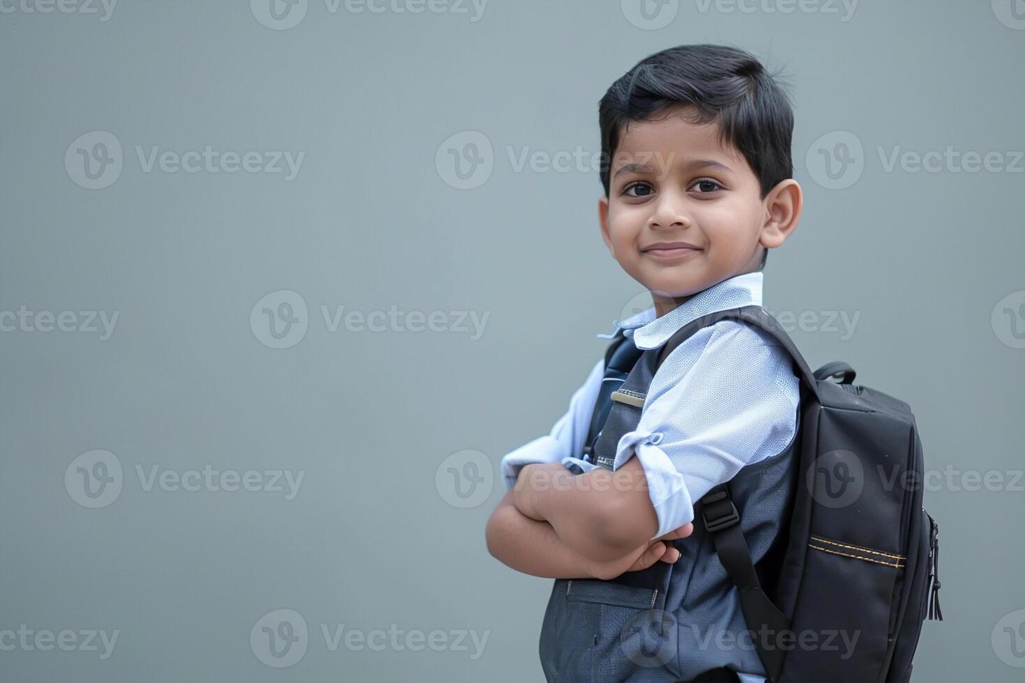 Back to school. A happy boy kid in school uniform, standing with hands crossed folded against isolated gray background. school kid photo