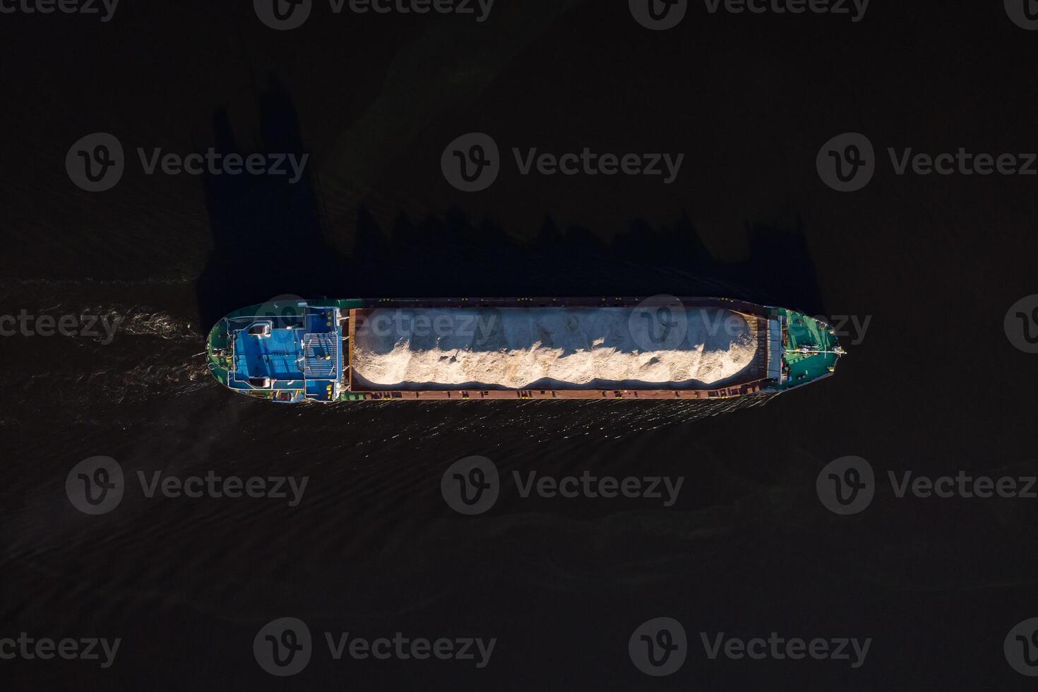 An aerial drone photo of a container cargo ship carrying load in colorful containers cruising in blue sea.