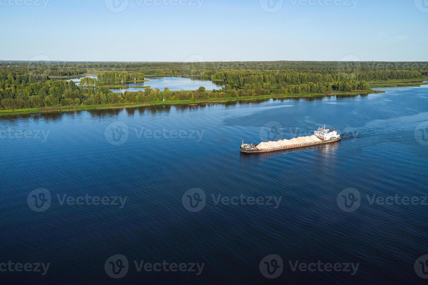 An aerial drone photo of a container cargo ship carrying load in colorful containers cruising in blue sea.