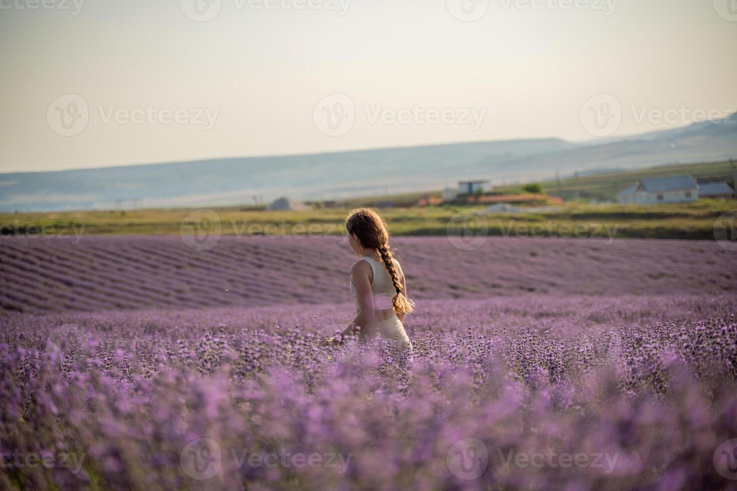 A girl stands in a field of purple flowers lavander. The sky is blue and the sun is setting. photo