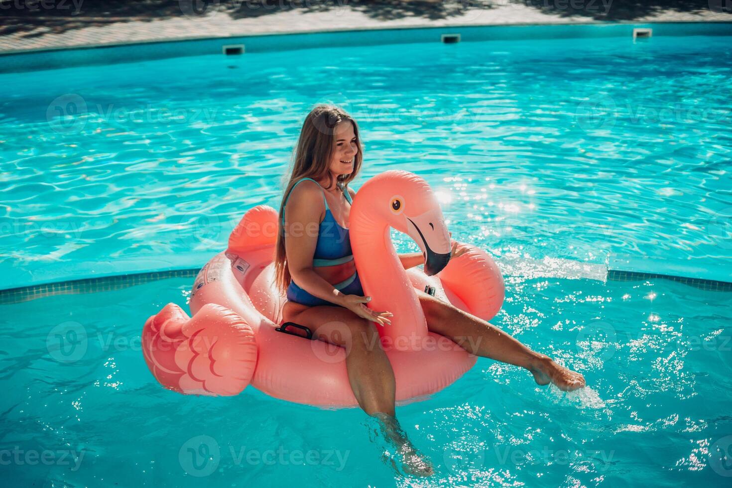 A woman is sitting on a pink inflatable flamingo in a pool. Concept of fun and relaxation, as the woman is enjoying her time in the water. photo