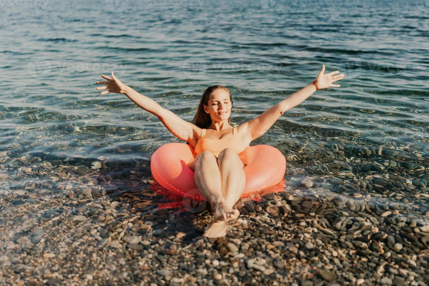 A woman is floating in a red inflatable raft on a rocky beach photo