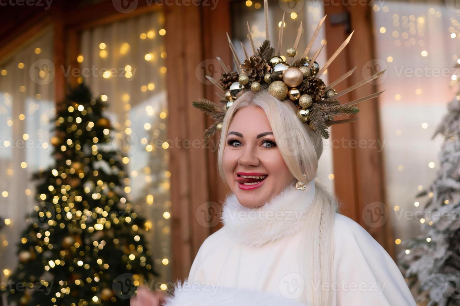 Happy blonde as Snow Maiden in white costume. Wooden house exterior Festive setting. Character with crown creating festive scene. photo