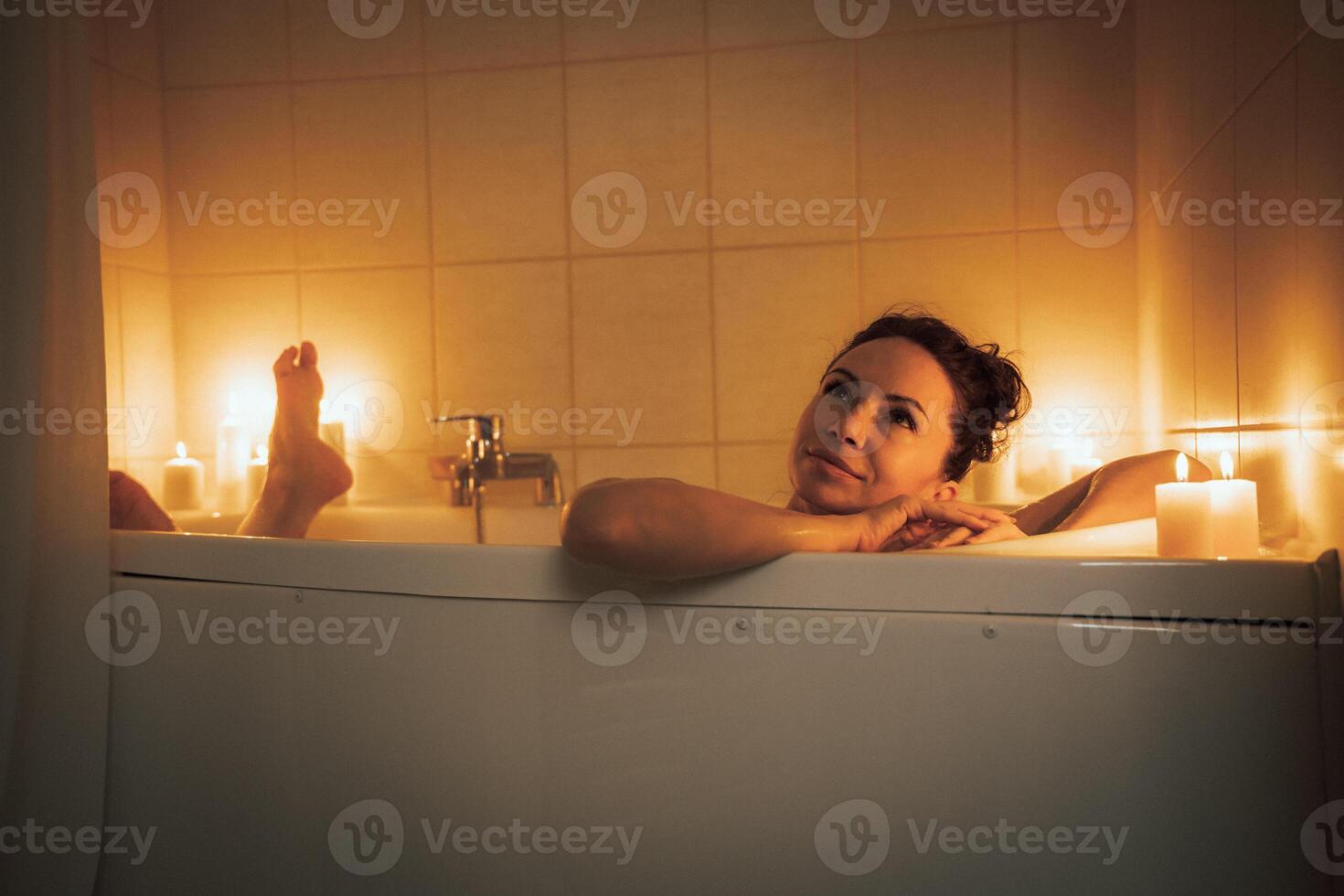 A woman is sitting in a bathtub with candles lit around her. She is smiling and she is enjoying her time. photo