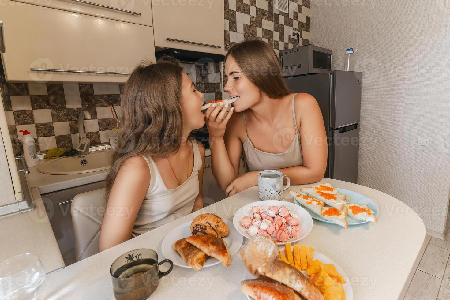 mom and daughter sitting at a table with a variety of food, including sandwiches, fruit, and pastries. They are smiling and enjoying their meal together. photo