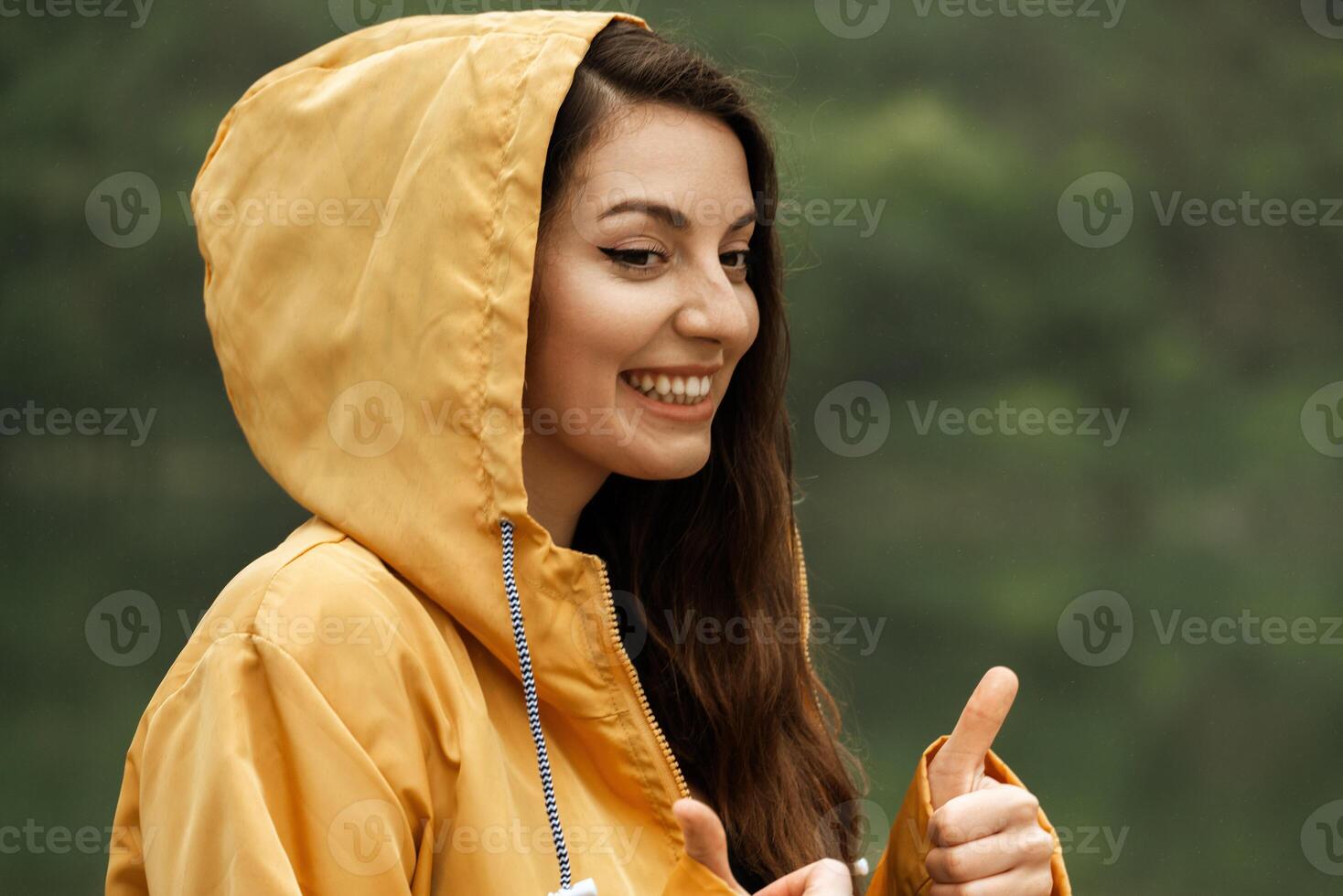 A woman in a yellow raincoat is smiling and giving a thumbs up photo
