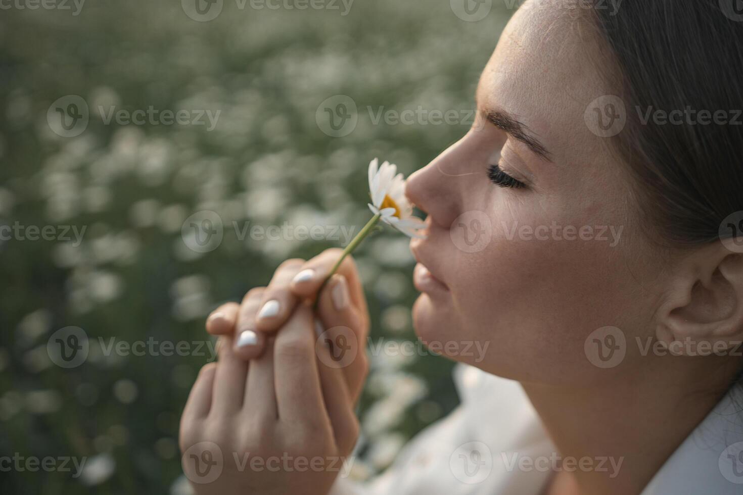 A woman is holding a flower and smelling it. Concept of peace and tranquility, as the woman takes a moment to appreciate the beauty of the flower. photo