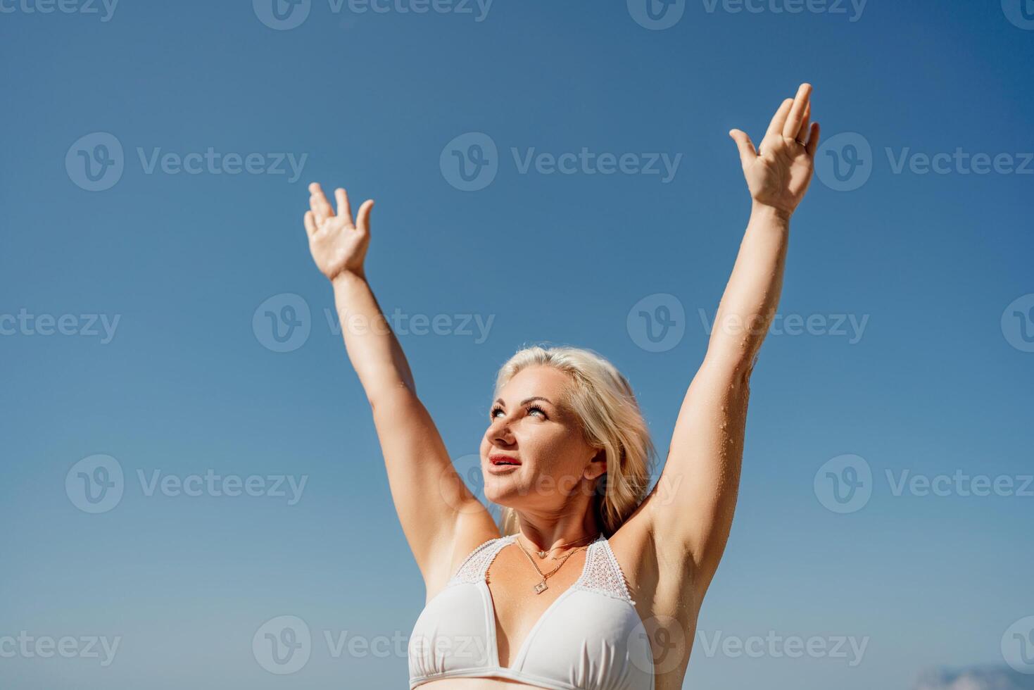 A woman is standing in the sun with her arms raised in the air photo