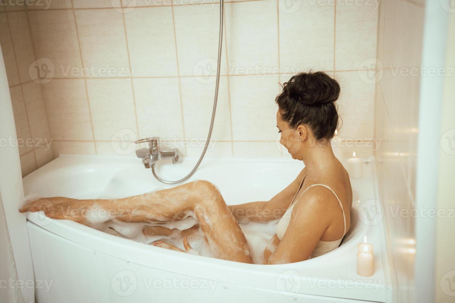 A woman is sitting in a bathtub with bubbles and candles. She is smiling and she is enjoying her bath. photo