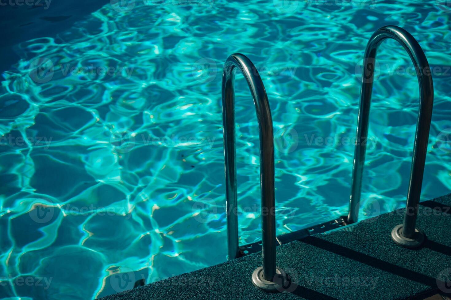 A metal ladder is in the water. The water is clear and calm. The ladder is in the middle of the pool. photo