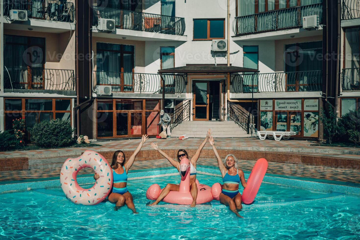 Three women are in a pool with inflatable toys, including a pink flamingo and a donut. photo