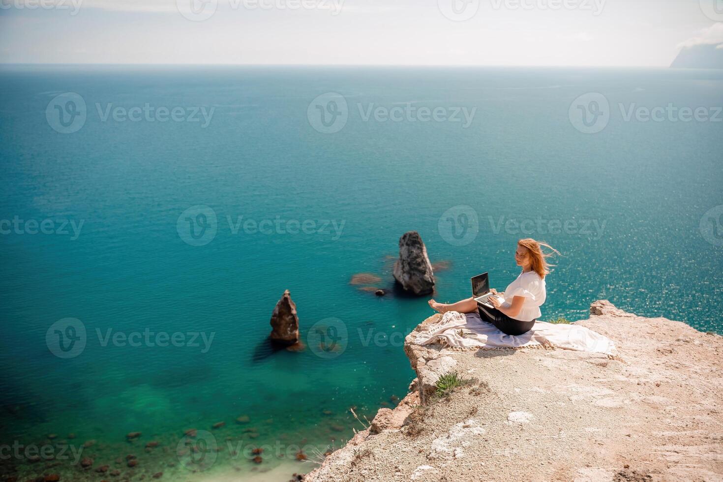 Freelance woman working on a laptop by the sea, typing away on the keyboard while enjoying the beautiful view, highlighting the idea of remote work. photo