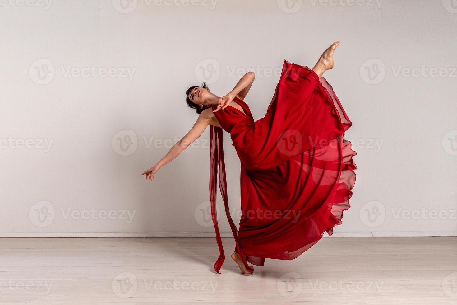 Dancer in a red flying dress. Woman ballerina dancing on a white studio background photo