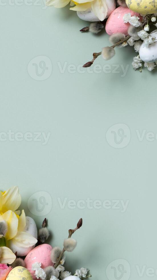 Daffodils, easter eggs and willow on green background with copy space. Easter greeting card template vertical format photo