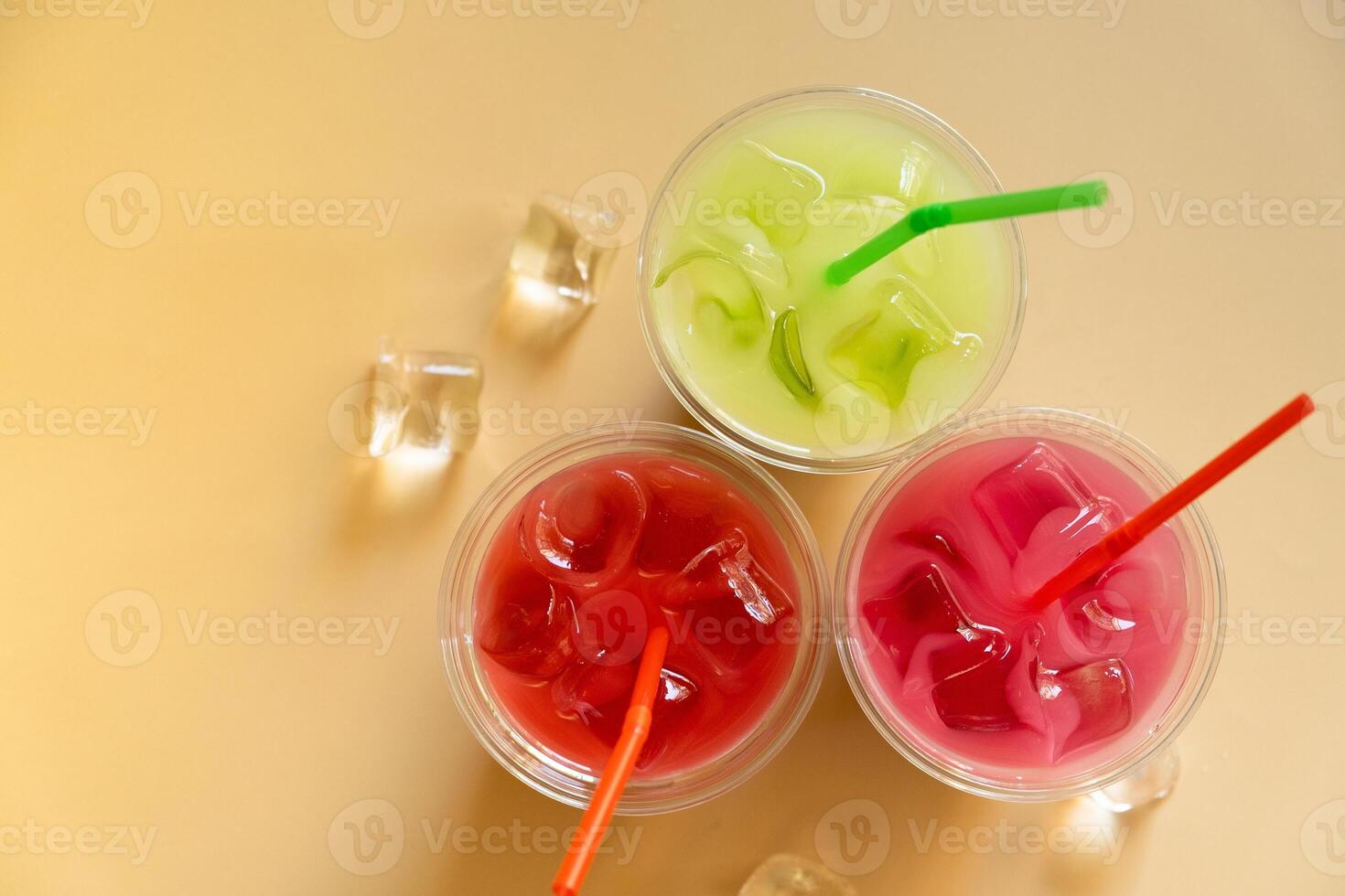 Colored summer lemonades on beige background with ice cubes photo