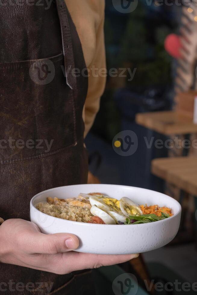 Bowl with dish in the hand of waiter in apron. Concept of healthy balanced nutrition, service area photo