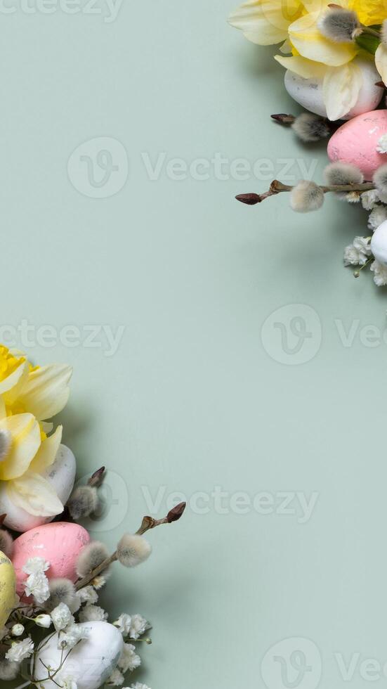 Daffodils, easter eggs and willow on green background with copy space. Easter greeting card template vertical format photo