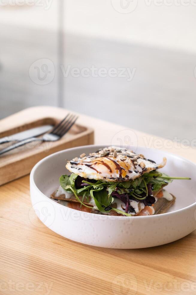 White plate with beautiful dish with salmon and egg and seeds angle view on wooden cafe table photo