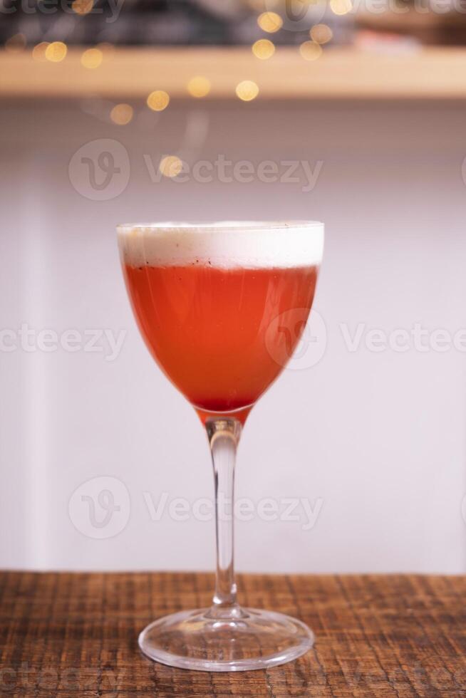 Red cocktail with whipped cream in glass on wooden table with bokeh photo