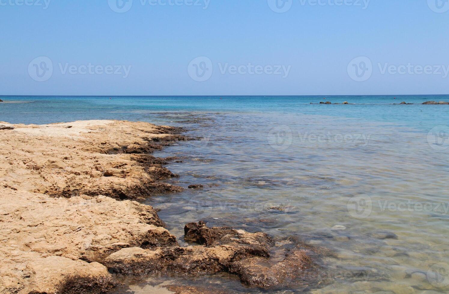 Rocky beach of the Mediterranean Sea, seaside resort of Cyprus island, Protaras. The stones are visible from the clear sea water on a sunny summer day. Natural daylight. Natural wallpaper photo