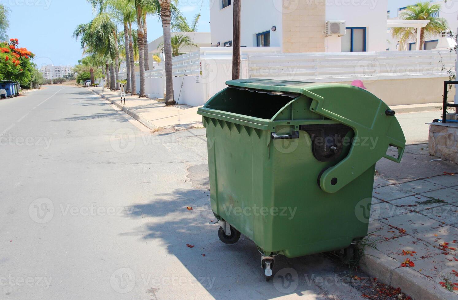 Green plastic trash container, trash can in the middle of the street. Reservoir for collecting, sorting and processing waste. Waste tank on a rotary on the street of Cyprus photo