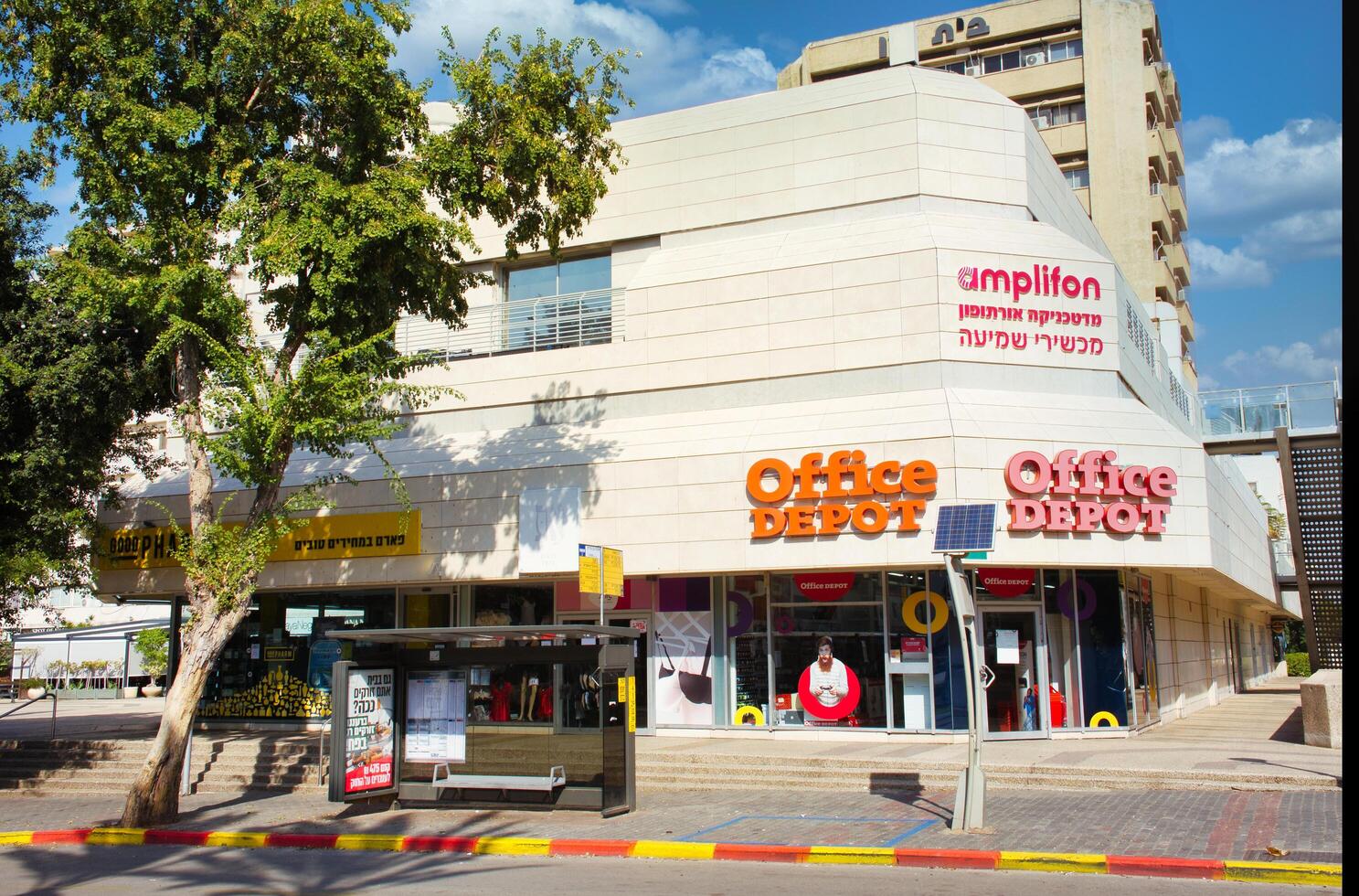 Raanana, Israel, November 12, 2022. Office Depot store exterior, green tree and bus stop. photo