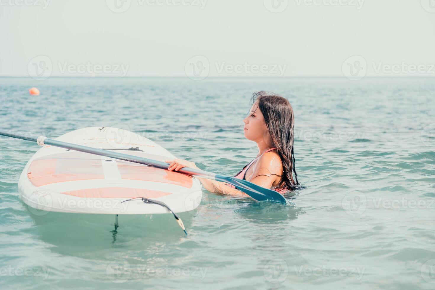 Sea woman sup. Silhouette of happy young woman in pink bikini, surfing on SUP board, confident paddling through water surface. Idyllic sunset. Active lifestyle at sea or river. photo