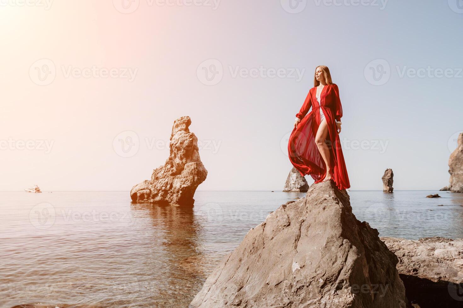 Woman travel sea. Young Happy woman in a long red dress posing on a beach near the sea on background of volcanic rocks, like in Iceland, sharing travel adventure journey photo