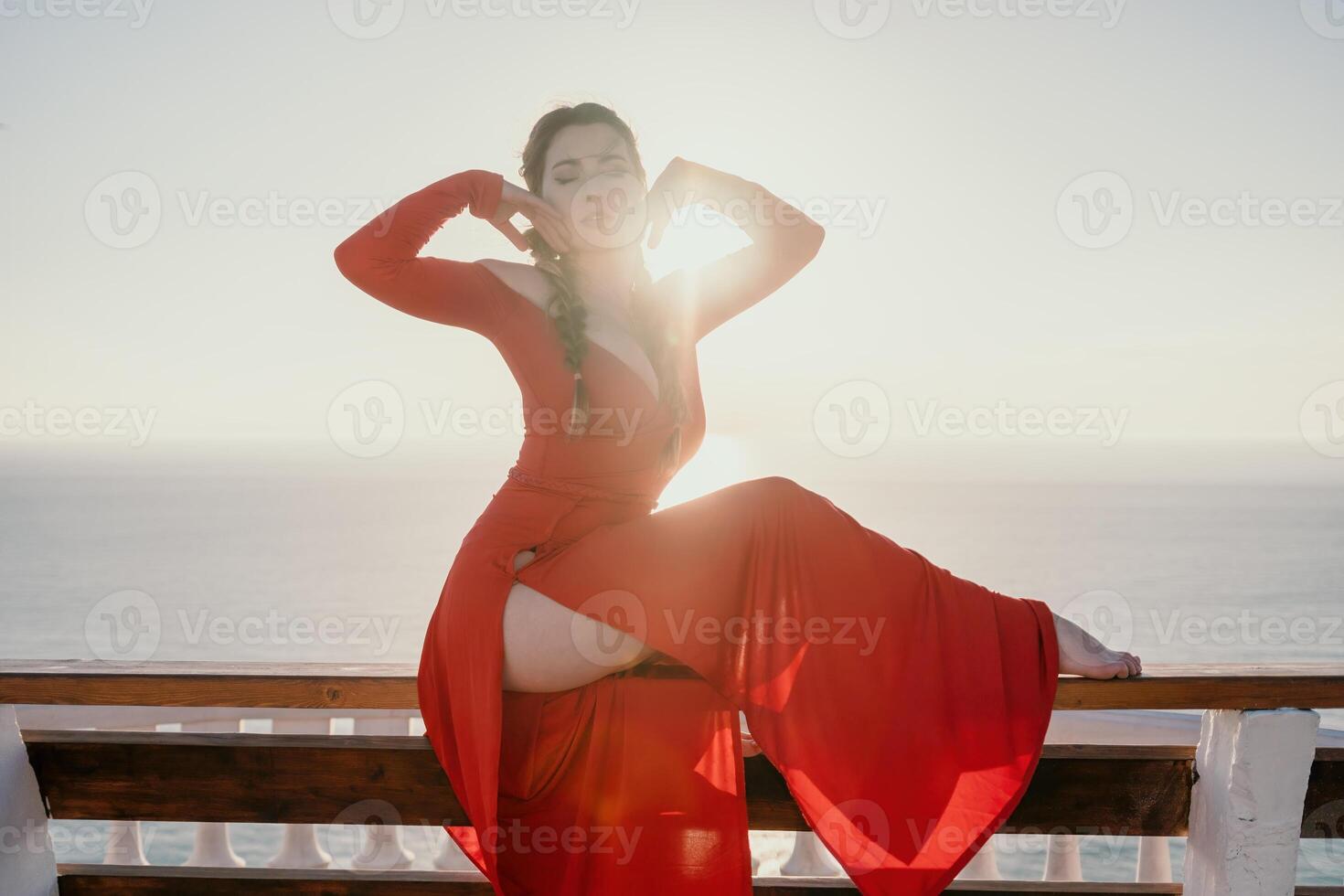 Closeup portrait of sensual young brunette woman in red dress, happily dancing outdoors isolated on blurry sea background with natural bokeh in soft warm sunset backlight. Selective focus. photo