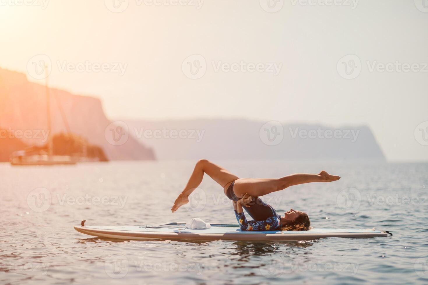 Woman sup yoga. Middle age sporty woman practising yoga pilates on paddle sup surfboard. Female stretching doing workout on sea water. Modern individual female hipster outdoor summer sport activity. photo