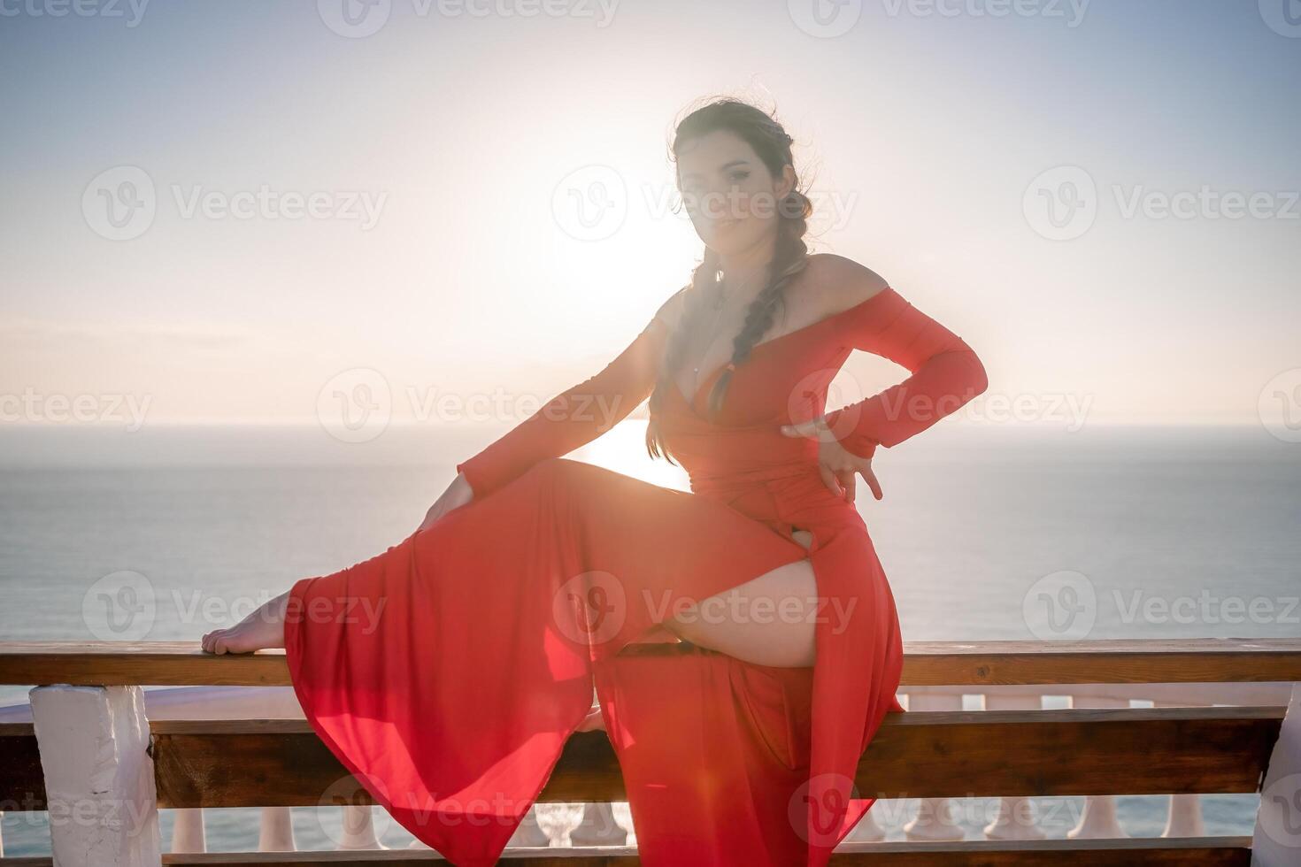 Closeup portrait of sensual young brunette woman in red dress, happily dancing outdoors isolated on blurry sea background with natural bokeh in soft warm sunset backlight. Selective focus. photo