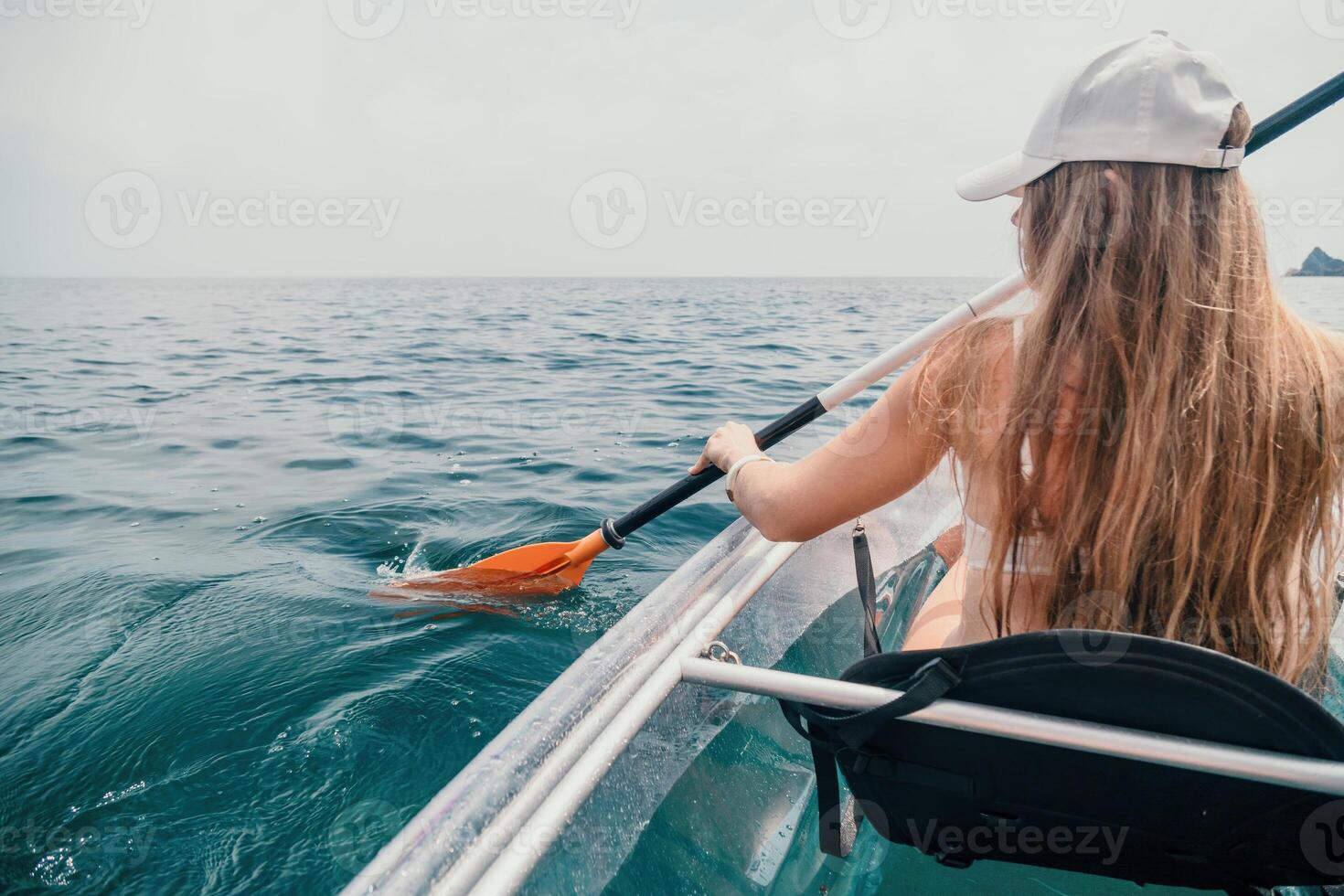 Woman in kayak back view. Happy young woman with long hair floating in transparent kayak on the crystal clear sea. Summer holiday vacation and cheerful female people relaxing having fun on the boat photo