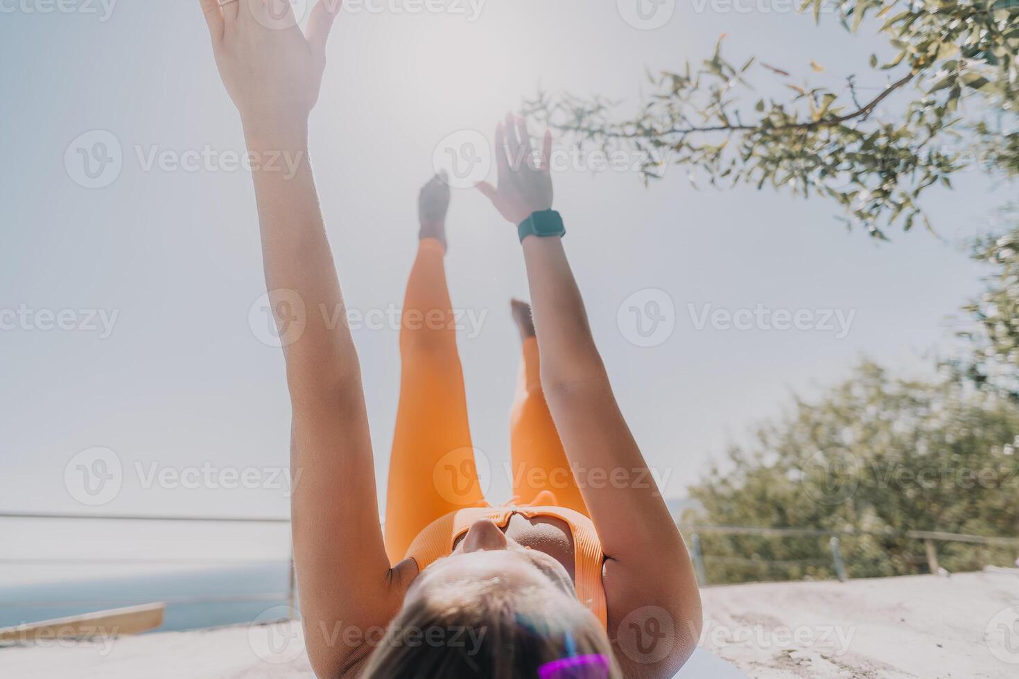 Fitness woman sea. Happy middle aged woman in orange sportswear exercises morning outdoors on yoga mat with laptop in park over ocean beach. Female fitness pilates yoga routine. Healthy lifestyle. photo