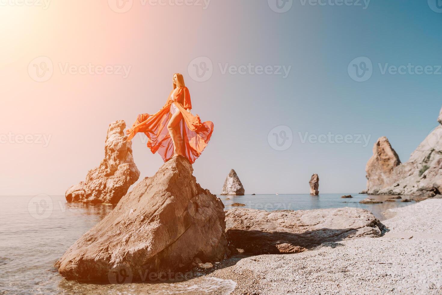 Woman travel sea. Young Happy woman in a long red dress posing on a beach near the sea on background of volcanic rocks, like in Iceland, sharing travel adventure journey photo