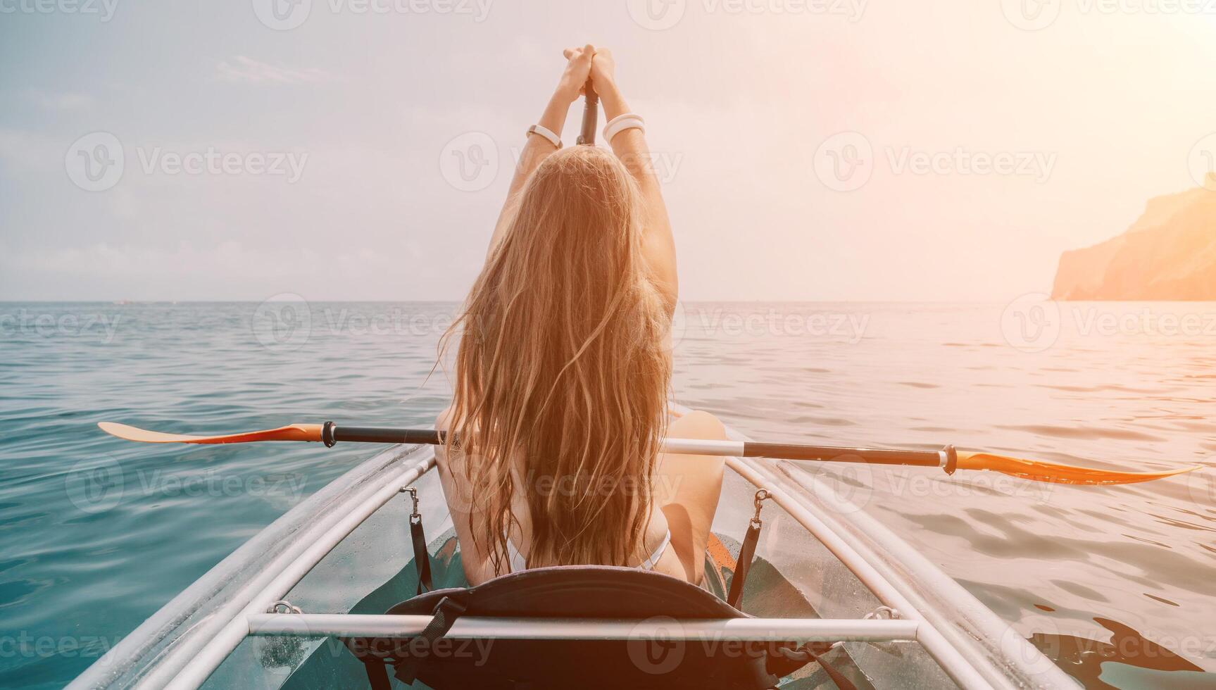 Woman in kayak back view. Happy young woman with long hair floating in transparent kayak on the crystal clear sea. Summer holiday vacation and cheerful female people relaxing having fun on the boat photo