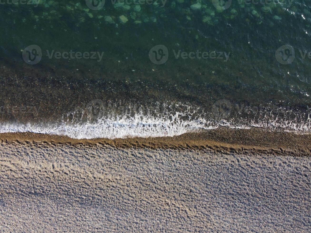 Aerial view from above on azure sea and pebbles beach. Small waves on cristal clear water surface in motion blur. Nature summer ocean sea beach background. Nobody. Holiday, vacation and travel concept photo