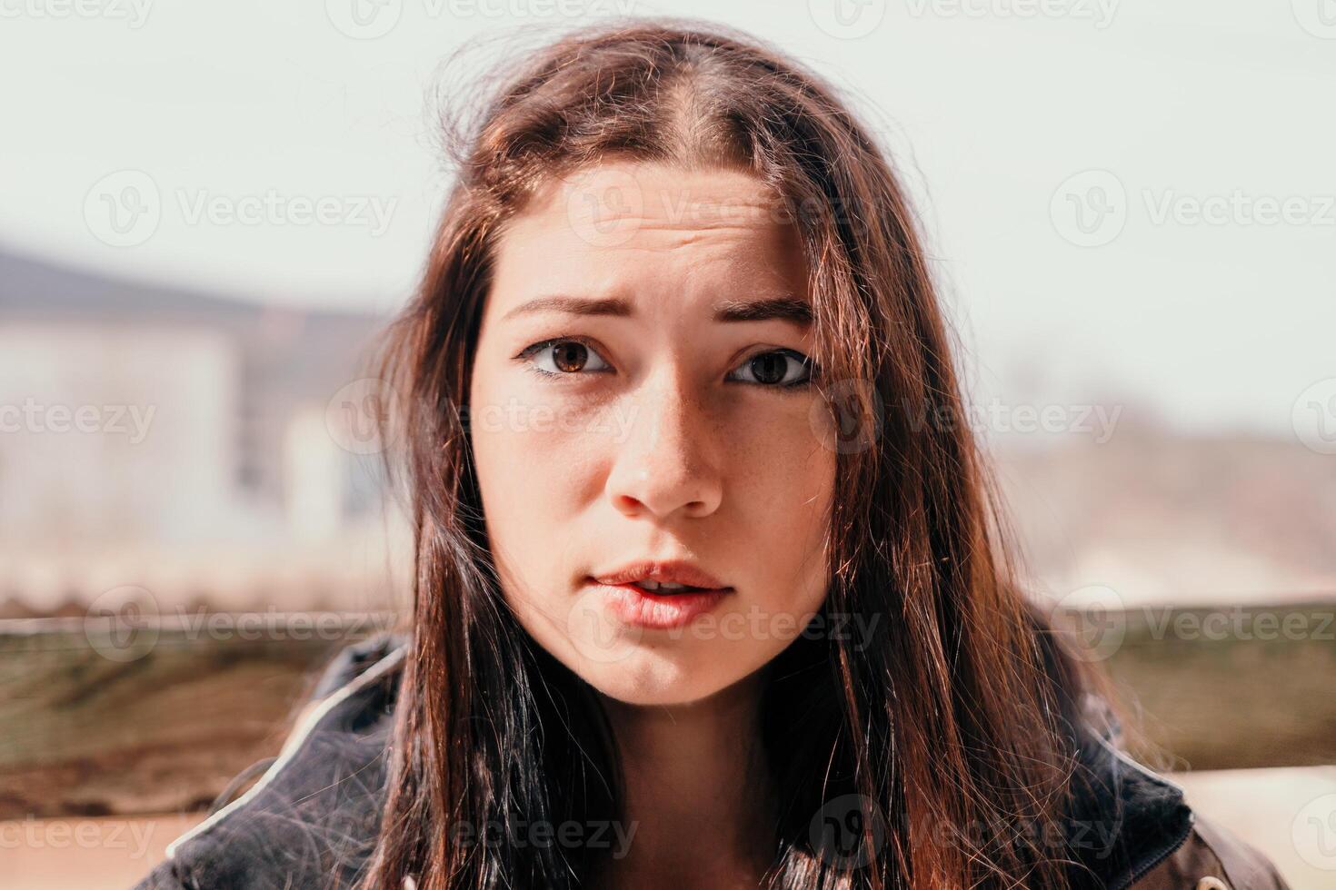 Happy young smiling woman with freckles outdoors portrait. Soft sunny colors. Outdoor close-up portrait of a young brunette woman and looking to the camera, posing against autumn nature background photo