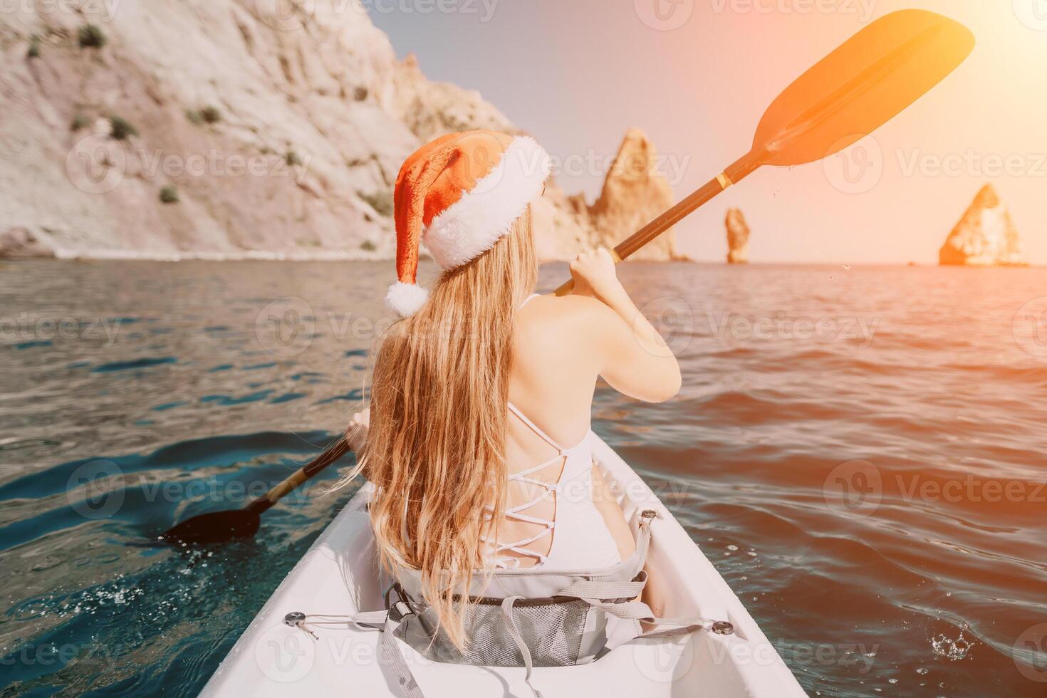 Woman in kayak back view. Happy young woman in Santa hat floating in kayak on calm sea. Summer holiday vacation and cheerful female people relaxing having fun on the boat. photo