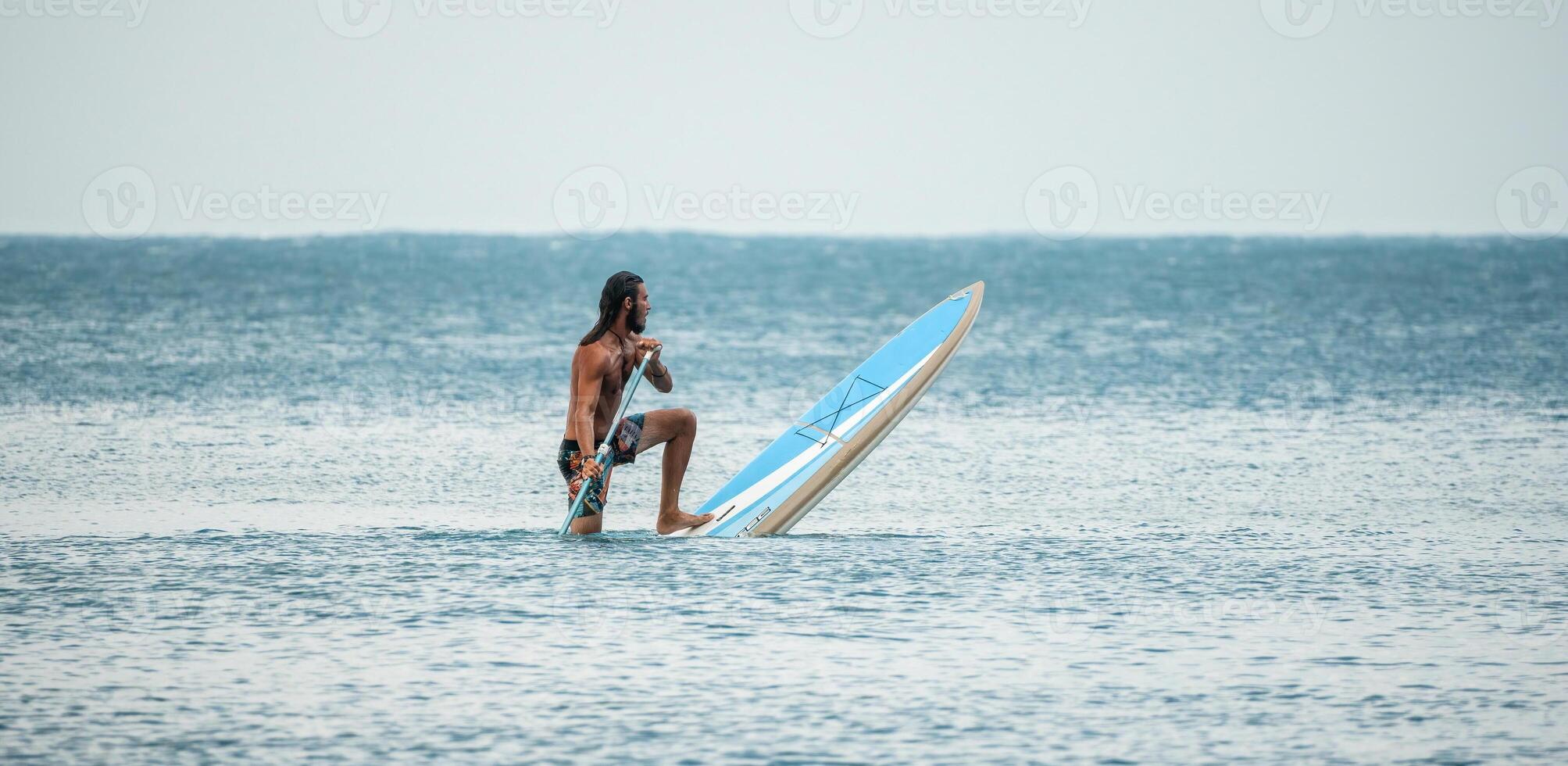 Sea man sup. Asian athlete man swimming in sea and paddleboarding at summer sunset. Healthy strong male enjoy outdoor active lifestyle and water sports on holiday vacation. photo