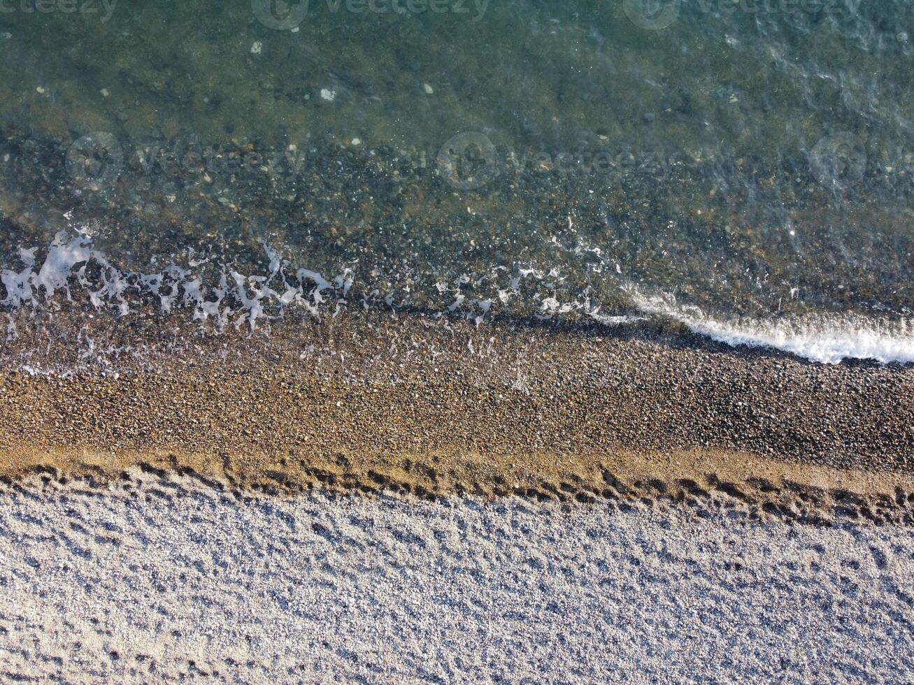 Aerial view from above on azure sea and pebbles beach. Small waves on cristal clear water surface in motion blur. Nature summer ocean sea beach background. Nobody. Holiday, vacation and travel concept photo