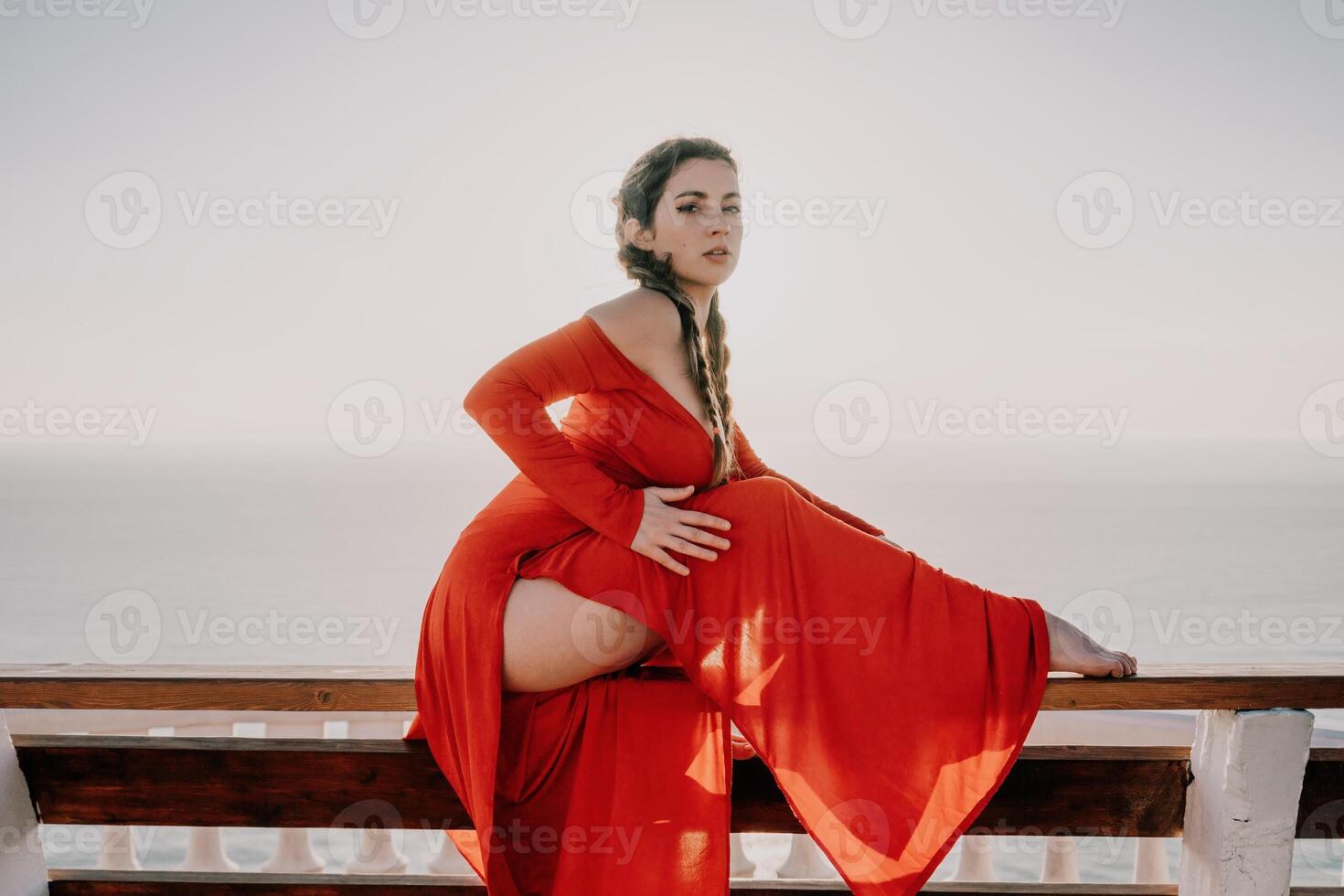 Closeup portrait of sensual young brunette woman in red dress, happily dancing outdoors isolated on blurry sea background with natural bokeh in soft warm sunset backlight. Selective focus. photo