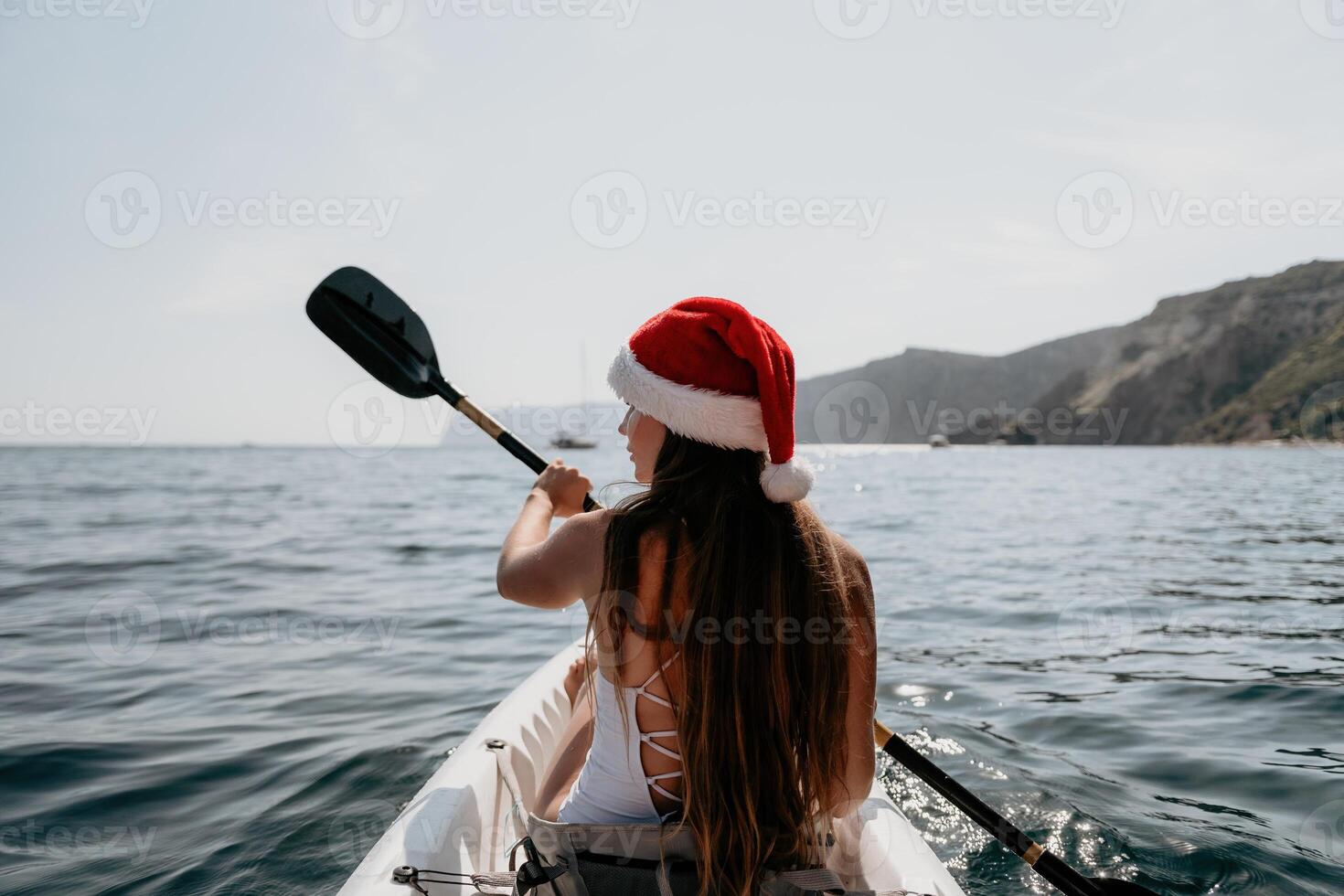Woman in kayak back view. Happy young woman in Santa hat floating in kayak on calm sea. Summer holiday vacation and cheerful female people relaxing having fun on the boat. photo