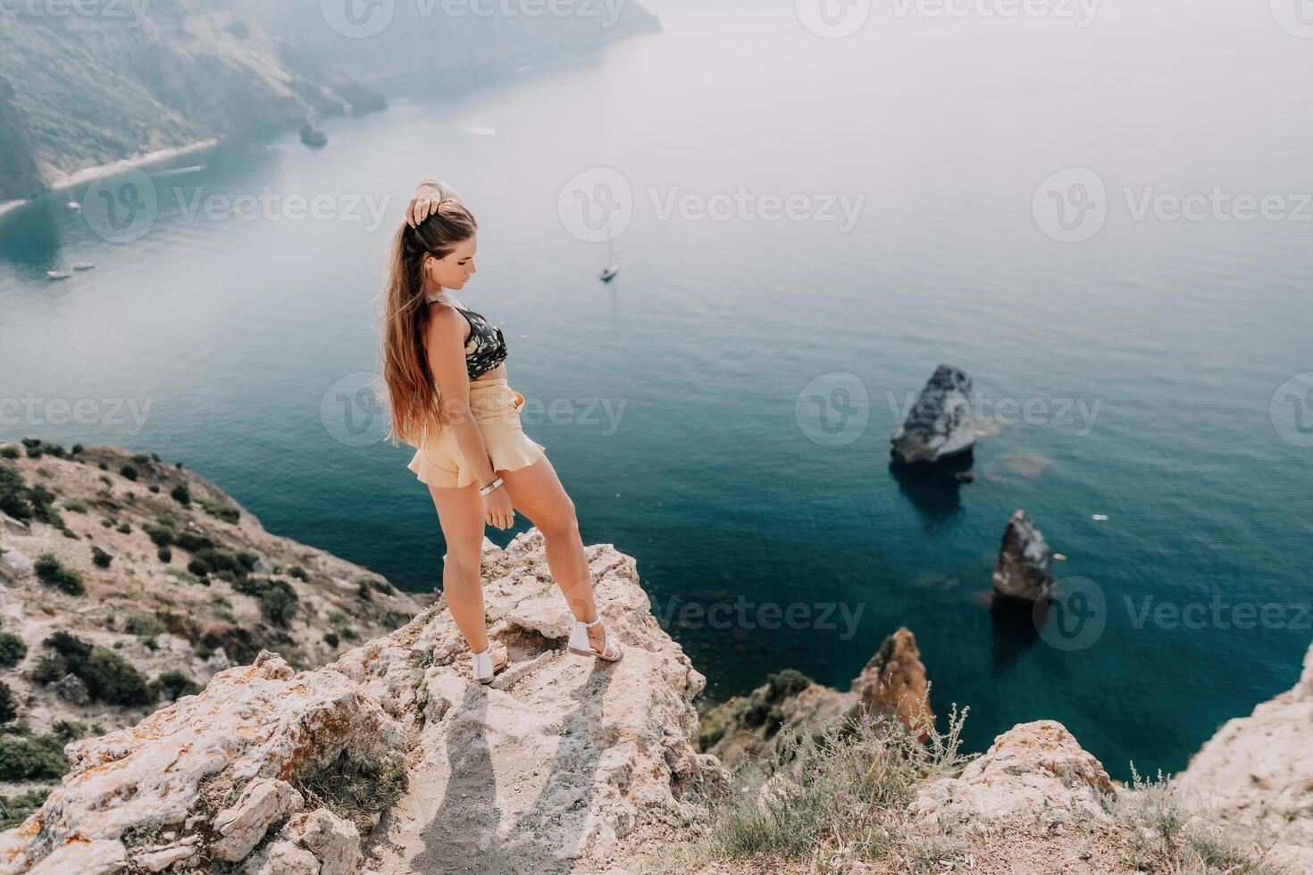 Woman travel sea. Happy tourist enjoy taking picture outdoors for memories. Woman traveler looks at the edge of the cliff on the sea bay of mountains, sharing travel adventure journey photo