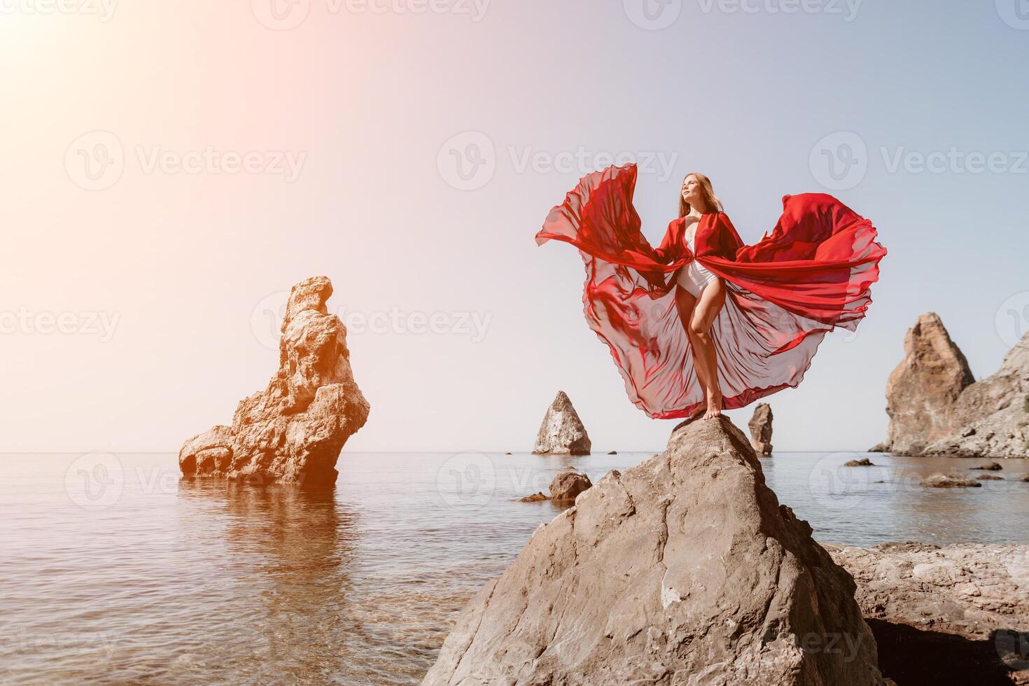 Woman travel sea. Young Happy woman in a long red dress posing on a beach near the sea on background of volcanic rocks, like in Iceland, sharing travel adventure journey photo
