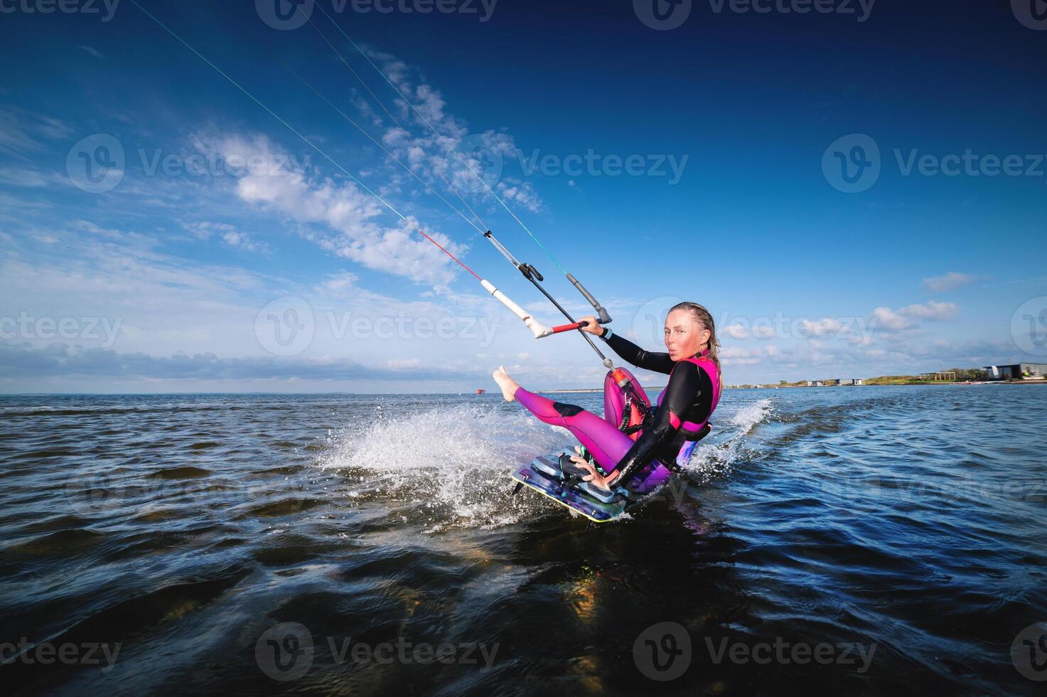 A young Caucasian woman in a wetsuit rides a kiteboard. An athlete performs a trick while sitting on a board with a kissing grimace. Beauty and grace in water sports photo