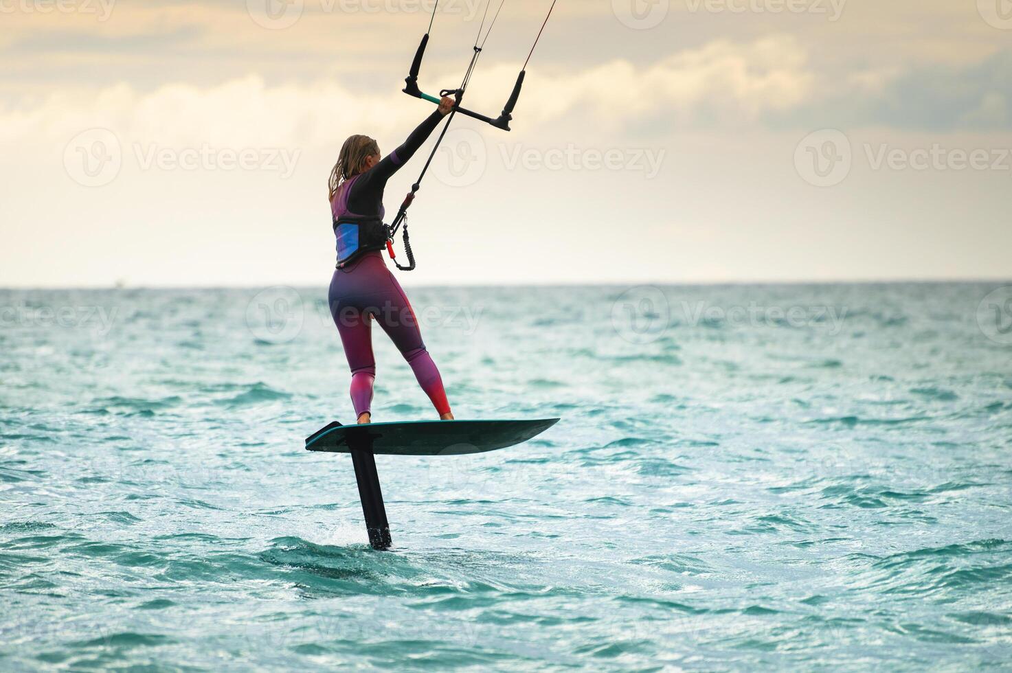 Young Caucasian woman athlete ride on a hydrofoil board with a kite in the open ocean. Hydrofoil is a new direction in kitesurfing photo