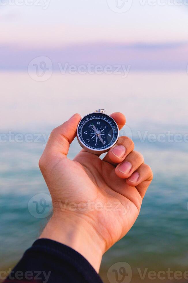 Navigation compass in a man's hand against the background of the sea, tourist compass first person view photo